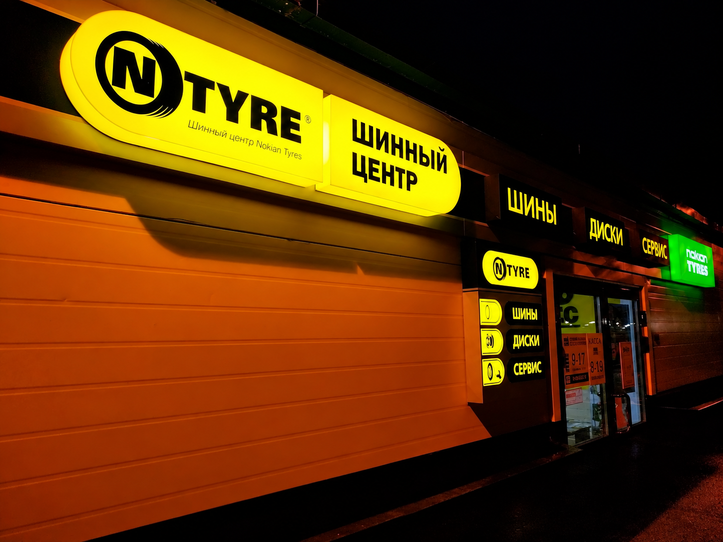 Жёлтые световые вывески на фасаде шинного центра